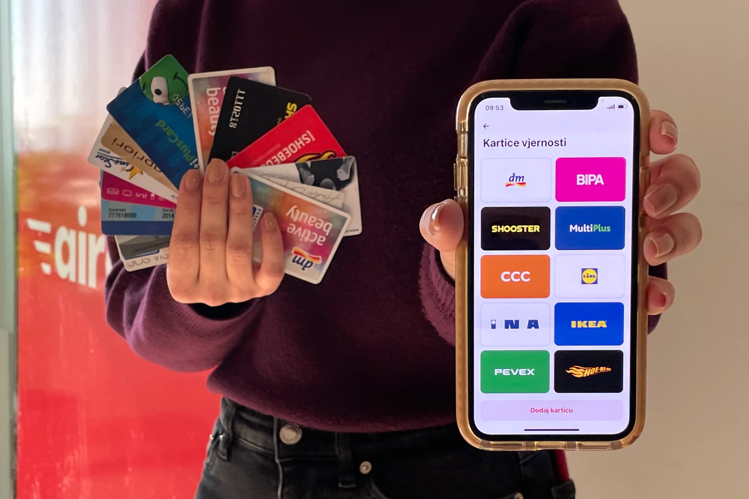 Person holding multiple loyalty cards in one hand and a smartphone displaying digital loyalty cards from various stores in the other hand.